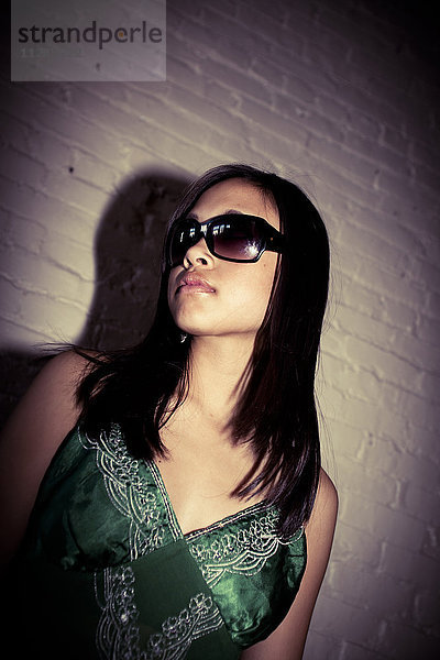 Glamouröses asiatisches Mädchen mit Sonnenbrille in der Nähe einer Backsteinmauer