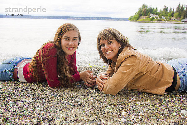 Lächelnde Mutter und Tochter liegen am felsigen Strand