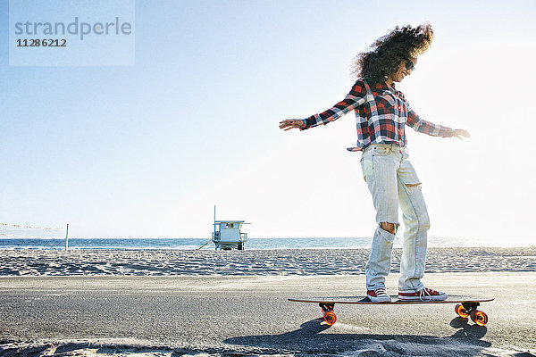 Hispanische Frau fährt Skateboard am Strand