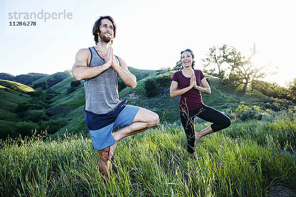 Lächelndes Paar übt Yoga auf einem Hügel
