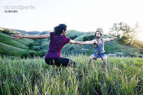 Paar hält sich an den Händen und praktiziert Yoga auf einem Hügel