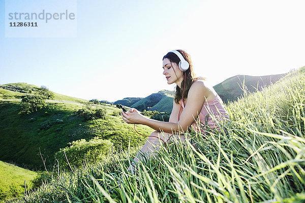 Kaukasische Frau sitzt auf einem Hügel und hört Kopfhörer