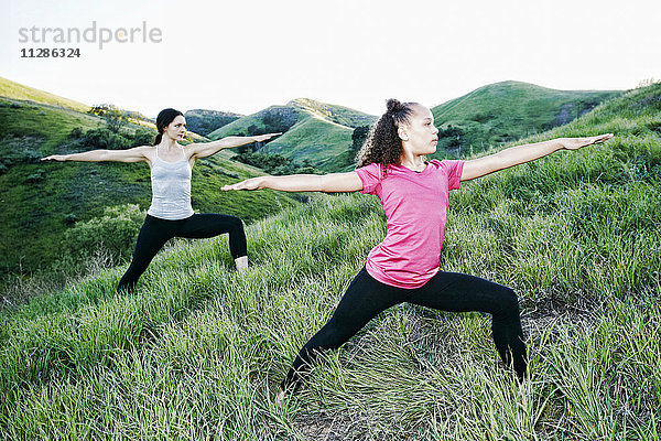 Mutter und Tochter üben Yoga auf einem Hügel