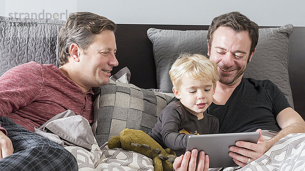 Kaukasische Väter benutzen ein digitales Tablet im Bett mit ihrem Sohn