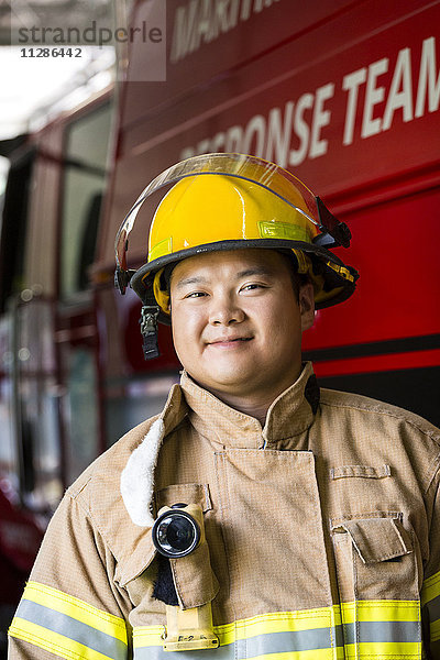 Lächelnder chinesischer Feuerwehrmann  der in der Nähe des Feuerwehrautos steht