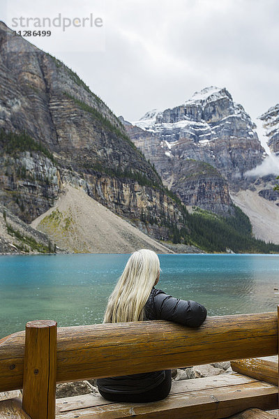 Weiße Frau sitzt auf einer Bank am Bergsee