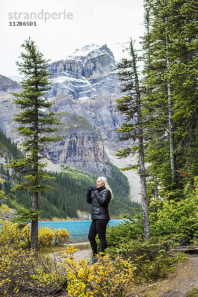 Kaukasische Frau mit Fernglas am Bergsee