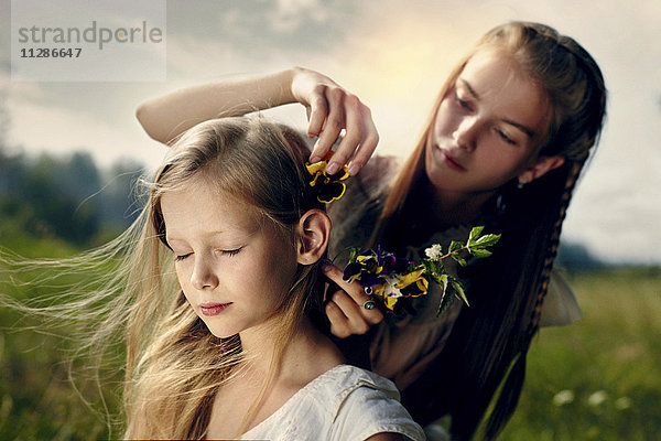 Kaukasisches Mädchen platziert Blume im Haar der Schwester