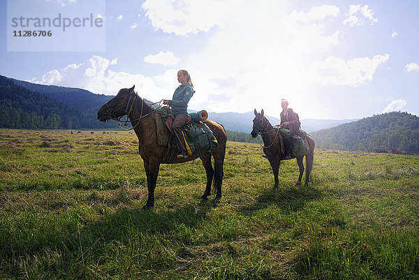 Kaukasische Mädchen reiten Pferde im Feld