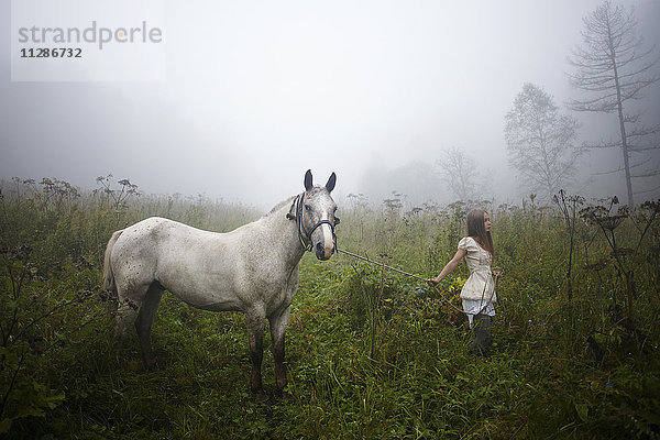 Kaukasisches Mädchen geht mit Pferd im nebligen Feld spazieren