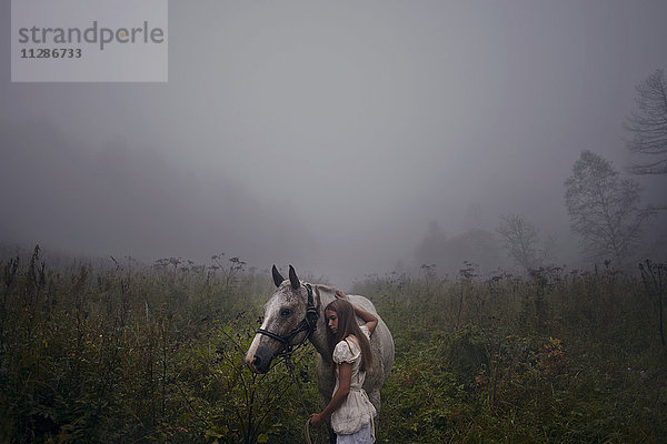 Kaukasisches Mädchen streichelt Pferd im nebligen Feld