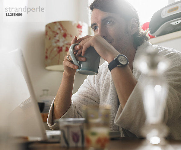 Porträt eines Mannes  der vor einem Laptop sitzt und eine Tasse hält
