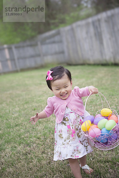 Kleinkind Mädchen läuft und lächelt mit vollem Ostereier-Bakset