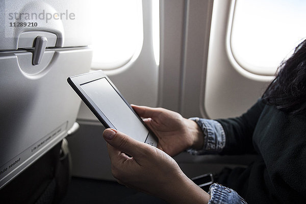Frau im Flugzeug sitzend mit E-Book  Teilansicht