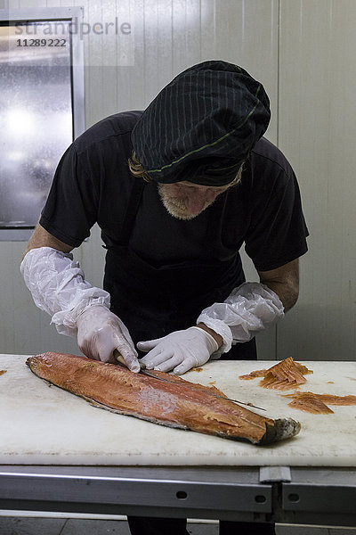 Fischraucher beim Reinigen von frisch geräuchertem Lachs mit einem Messer