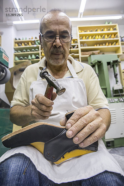 Schuhmacher bei der Arbeit mit dem Hammer am Schuh in seiner Werkstatt