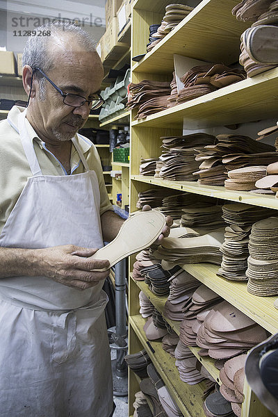 Schuhmacher wählt Schuhsohlen aus einem Regal in seiner Werkstatt aus.