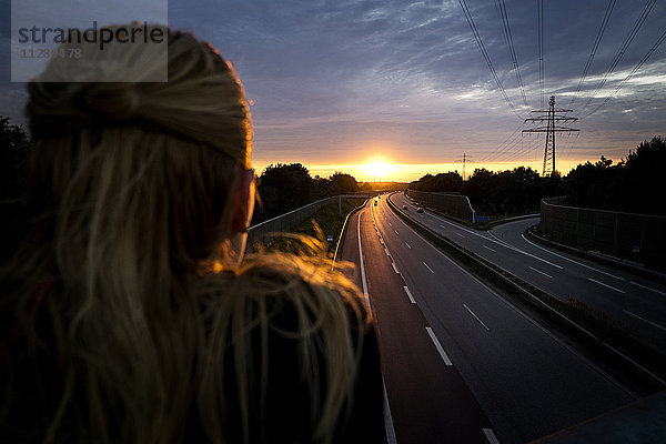 Frau bei Sonnenuntergang hinter der Autobahn