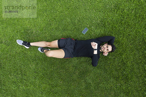 Jogger im Gras liegend mit Blick auf die Uhr