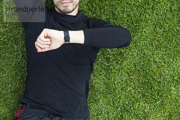 Jogger im Gras liegend mit Blick auf die Uhr