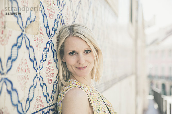 Portugal  Lissabon  Portrait einer lächelnden blonden Frau  die sich mit Azulejos an die Wand lehnt.