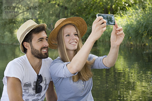 Lächelndes junges Paar an einem See mit einem Selfie
