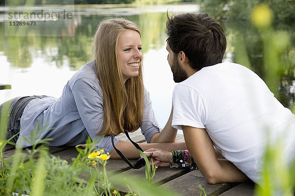 Lächelndes junges Paar auf einem Steg am See liegend