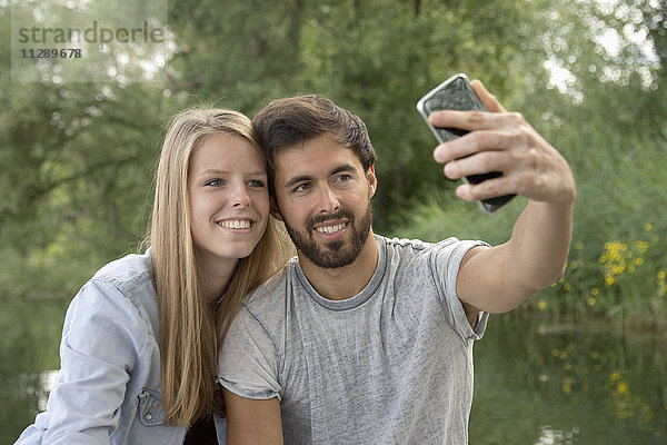 Lächelndes junges Paar an einem See mit einem Selfie