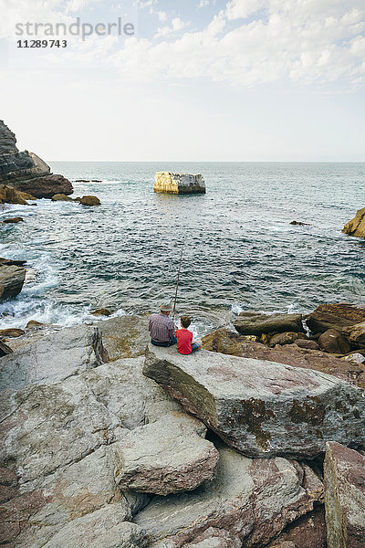 Großvater und Enkel beim gemeinsamen Fischen am Meer auf dem Felsen