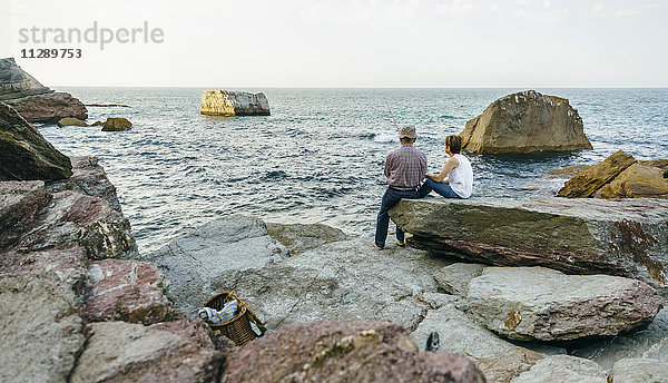 Seniorenpaar beim Fischen am Meer auf Felsen sitzend