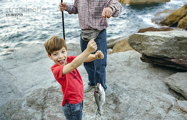 Glücklicher Junge hält Fisch an der Angelschnur  der von seinem Großvater gefangen wurde.