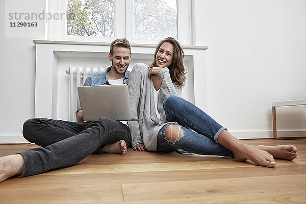 Lächelndes Paar auf dem Boden sitzend mit Laptop