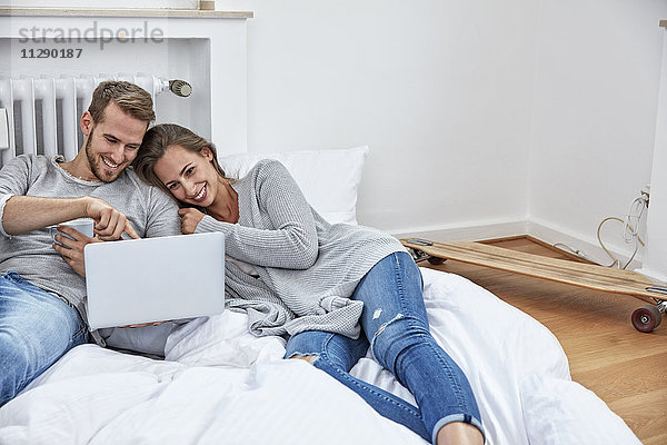 Lächelndes Paar auf Bettzeug auf dem Boden liegend mit Blick auf Laptop
