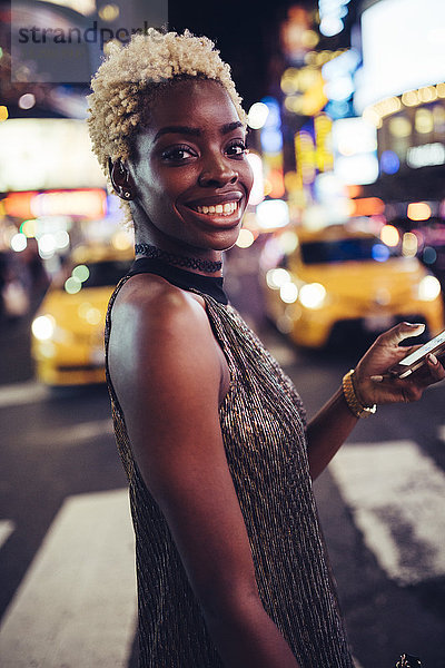 USA  New York City  Porträt einer lächelnden jungen Frau am Times Square bei Nacht
