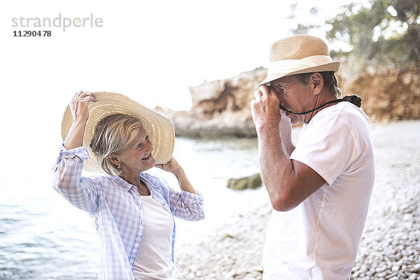 Älterer Mann beim Fotografieren seiner Frau am Strand