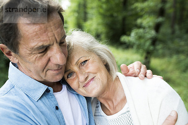 Porträt einer lächelnden Seniorin mit dem Kopf auf der Schulter ihres Mannes im Wald.