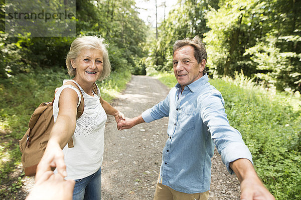 Seniorenpaar hält Hände mit dritter Person auf Waldweg