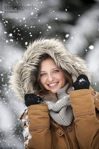 Junge Frau mit Fellkapuze im Schneefall  Portrait