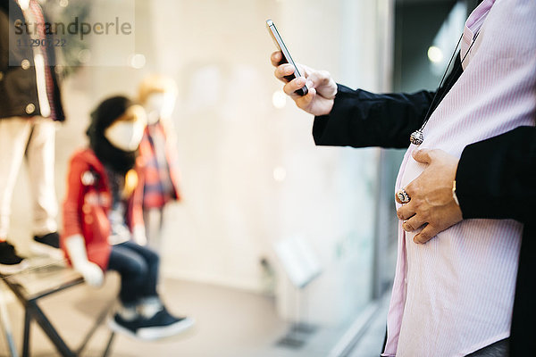 Schwangere mit Handy am Schaufenster