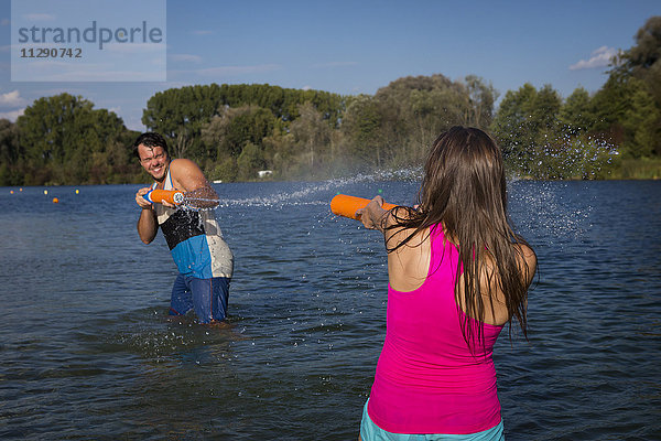 Junges Paar am See beim Spielen mit Wasserpistolen
