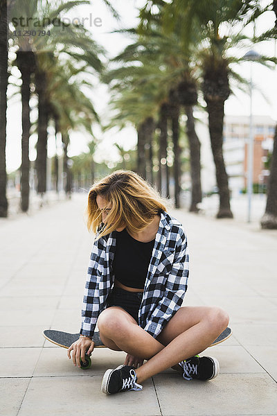 Spanien  junge Frau auf dem Skateboard sitzend