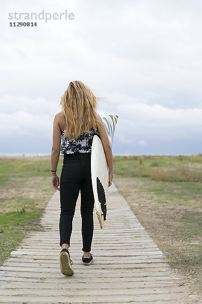 Rückansicht der jungen Frau mit Surfbrett auf Holzsteg