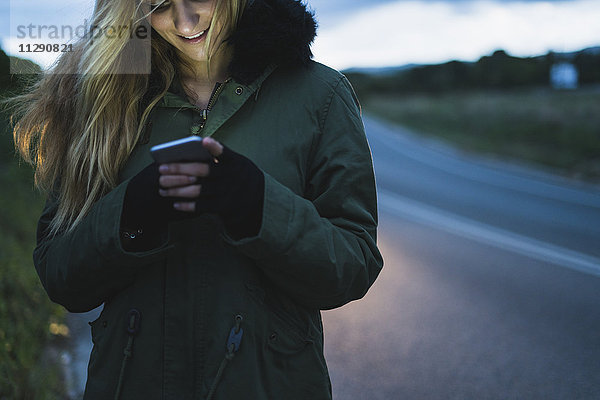 Lächelnde junge Frau SMS am Straßenrand
