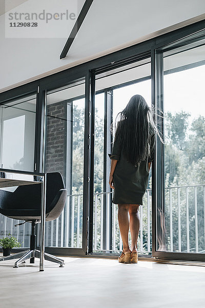Frau mit langen grauen Haaren aus dem Fenster schauend