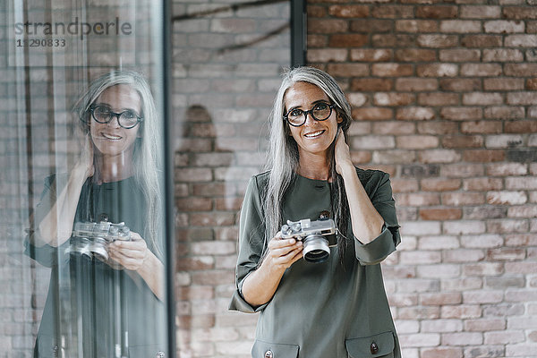 Porträt einer lächelnden Frau mit langen grauen Haaren  die eine Kamera hält.