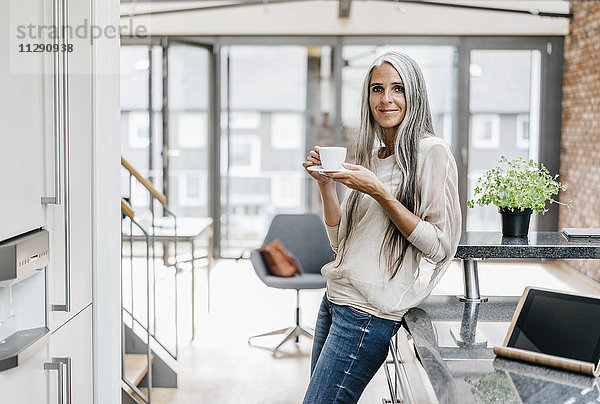 Lächelnde Frau mit langen grauen Haaren beim Kaffeetrinken