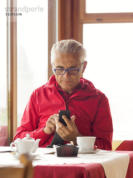 Ein älterer Mann sitzt in einem Café und benutzt ein Handy.