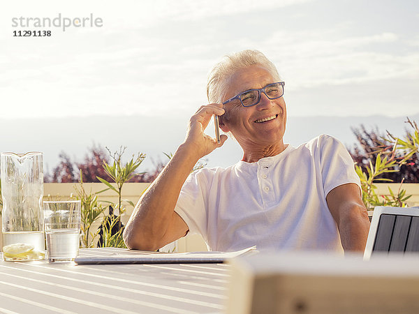 Glücklicher Senior am Telefon auf der Terrasse