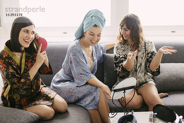 Drei junge Frauen sitzen auf der Couch und tragen Bademäntel  um sich auf den Tag vorzubereiten.