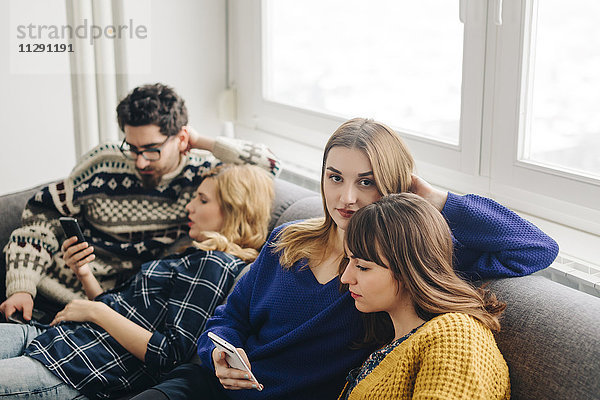 Vier Freunde mit Smartphones auf der Couch im Wohnzimmer hängen heraus